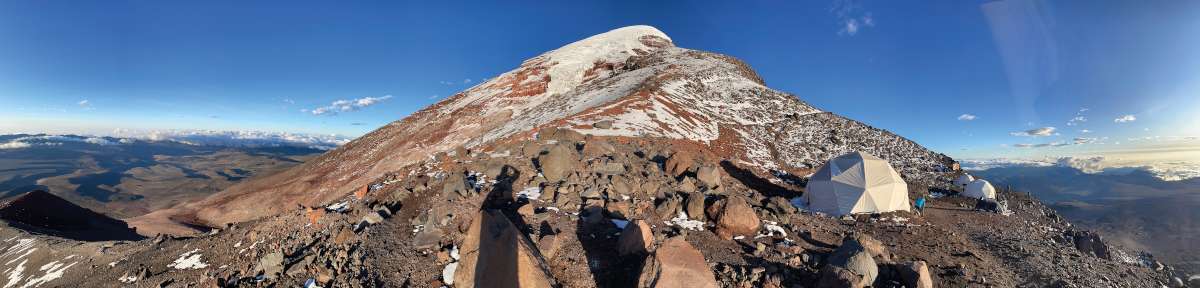 Nyugatról közelítve – Fent a vulkán sziklás vállán, 5300 m-en. Csalóka a látvány, mert innen még 6-8 óra mászást igénylő 1000 m-nyi emelkedő jön, ennek nagy része meredek, hasadékos gleccser. Csúcs valójában nincs is, a tetőszintet hatalmas, szeles, zord jégkupolák alkotják